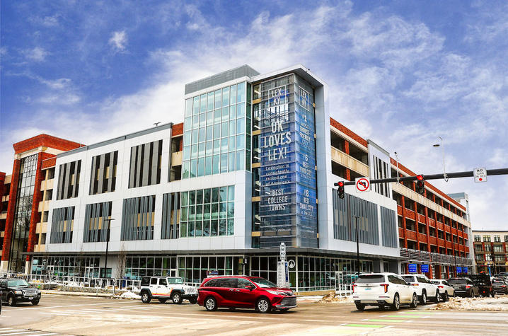 Modern multi-story campus building at a street corner, with large glass windows and parked cars.