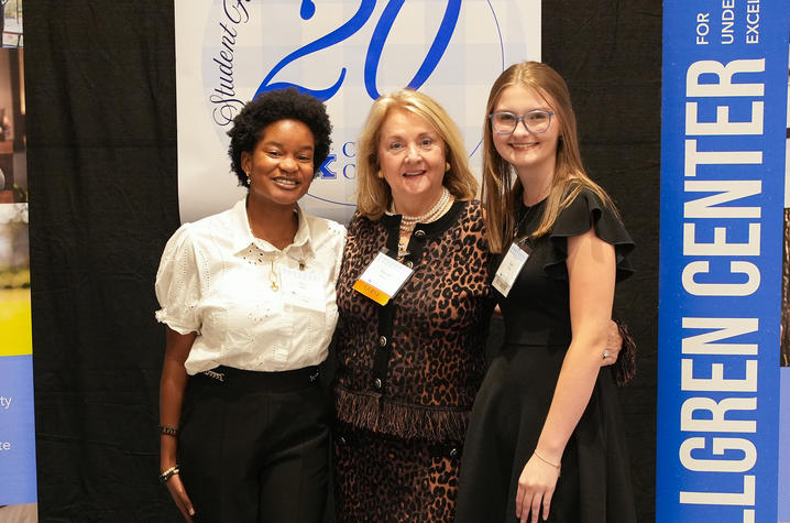 Three people pose together at an indoor event between banners, including one for the Gatton College Center.