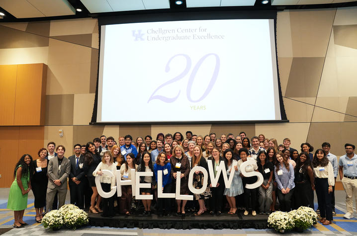 Group photo of UK fellows standing on a stage beneath a screen marking the program’s 20th anniversary.