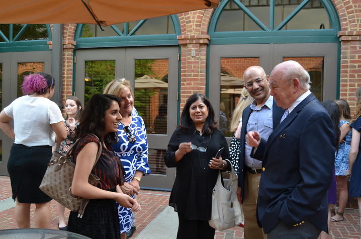 Several people stand and talk together during an outdoor gathering in front of a brick building.