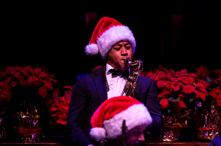 Male saxophone player wearing a black jacket and red and white Santa Claus hat