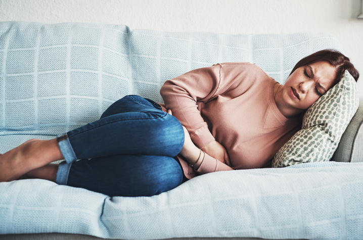 image of woman lying on sofa, holding her abdomen in pain