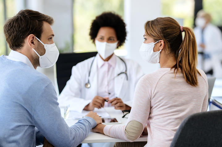 A husband and wife holding hands and looking at each other while sitting at a table talking to a doctor