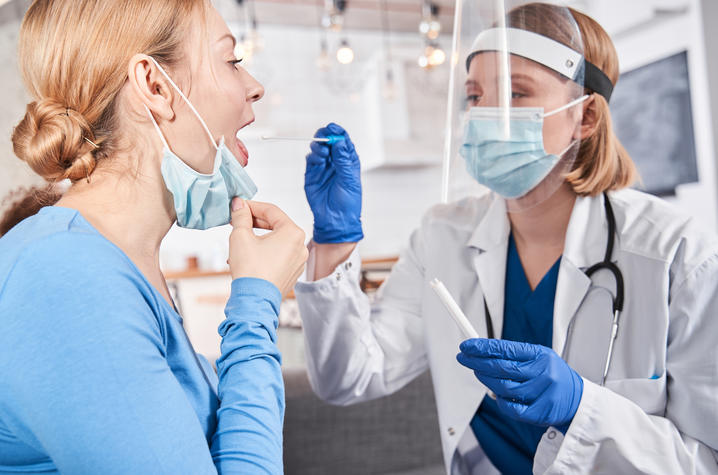 stock photo of health care professional in mask and shield swabbing young adult's mouth