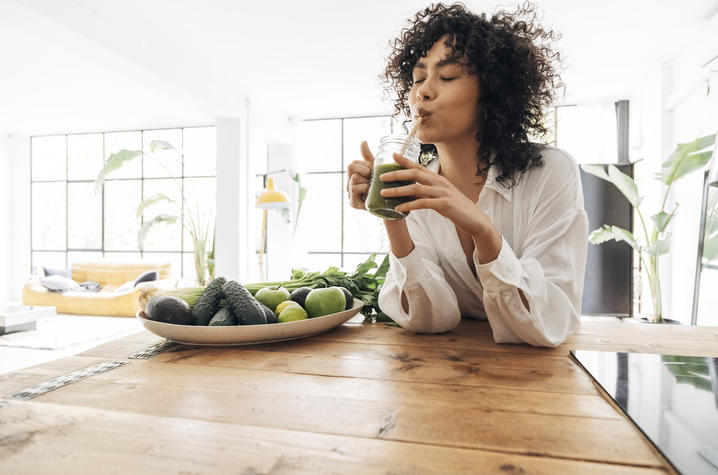 woman drinking green smoothie at counter