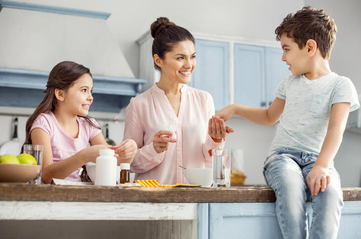 children in kitchen with mother giving vitamins