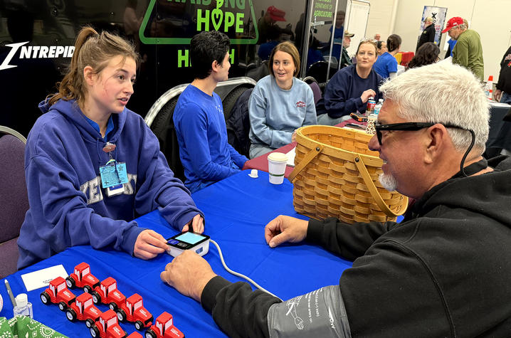 photo of Raising Hope People sit around a blue-covered table at a community event, engaging in an activity with small red-and-white items and a basket on the table.