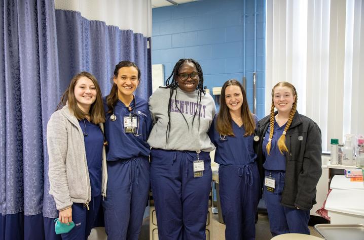 Image of five medical students in scrubs posing for a photo inside a clinic.