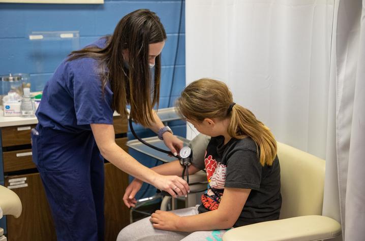 Photo of medical student in blue scrubs taking the blood pressure of a young girl.