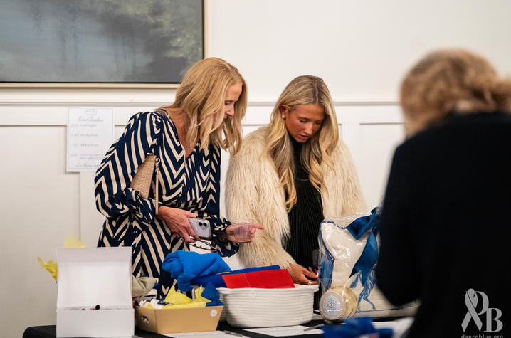 Two people look over blue, white and yellow items displayed on a table during an indoor event.