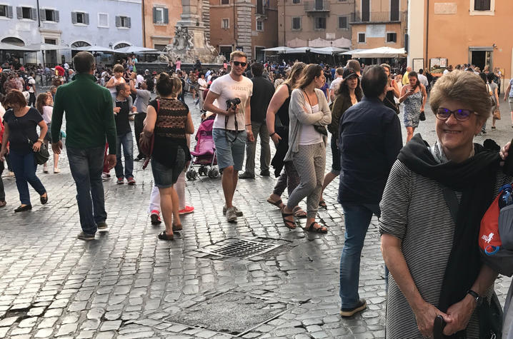 Geri standing on a crowded Italian street wearing a black and white striped top and black scarf.