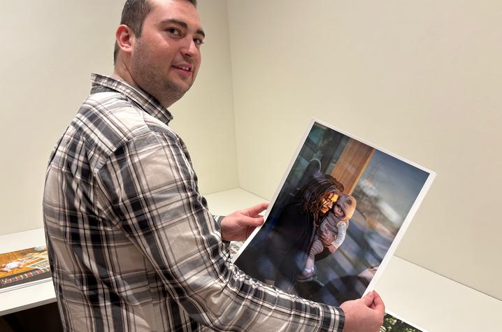 white male wearing a plaid shirt, holding a photo print, standing in a gallery with white walls