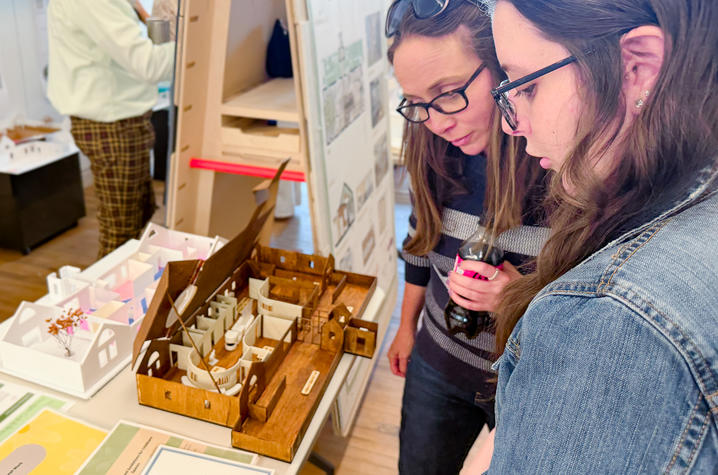Two people examine detailed architectural models displayed on a table at an exhibition.