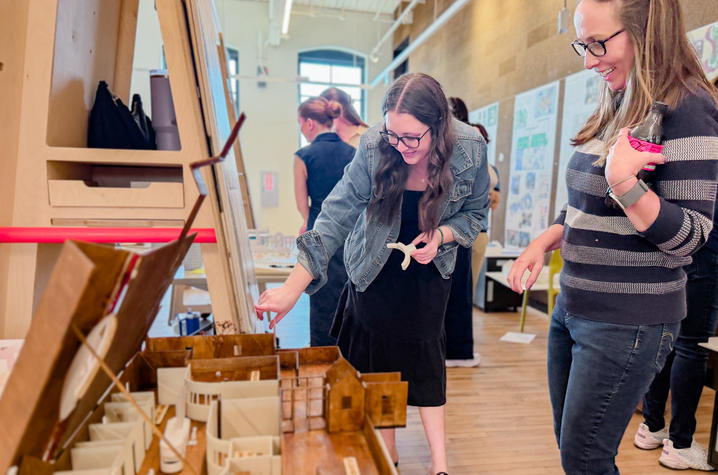 Two people smile as one points to a detailed architectural model at an exhibition.