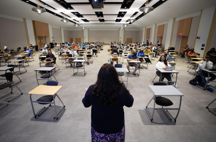 photo of professor at front of room speaking to in-person class of Journalism 101 students wearing masks and physically distant in the room.