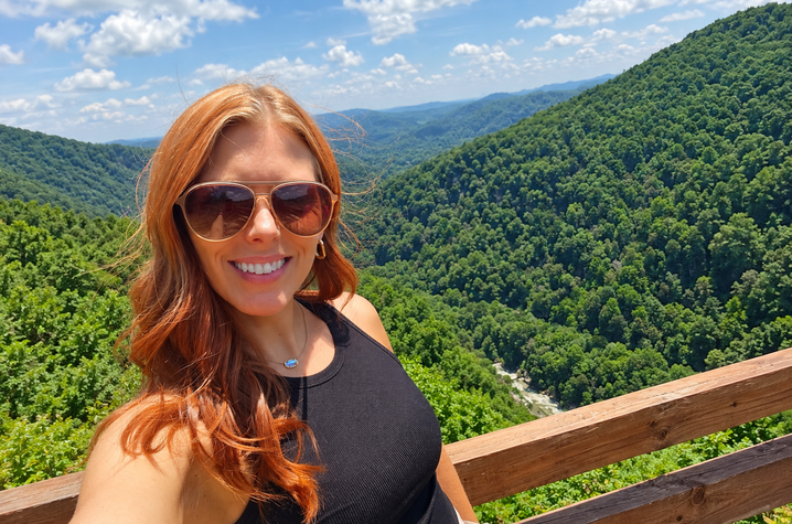 Photo of Latasha Friend A person wearing sunglasses stands at an overlook with green, forested Eastern Kentucky mountains in the background.
