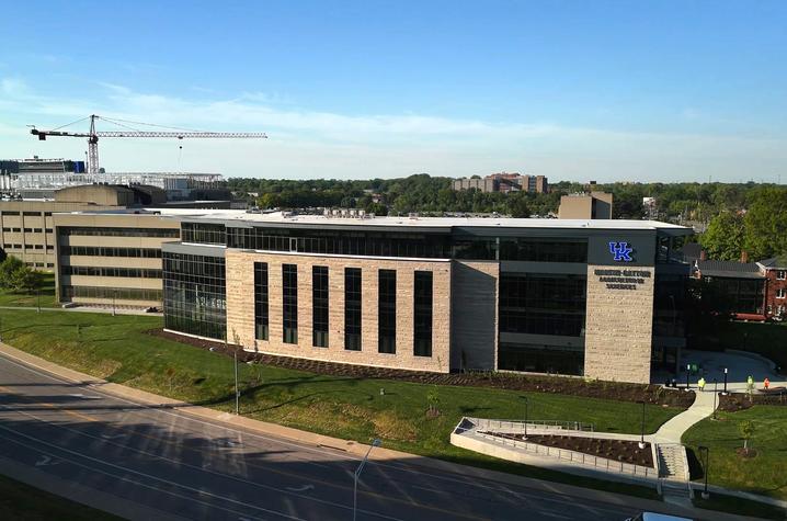 Aerial view of a modern University of Kentucky campus building beside a roadway, with surrounding green space and construction visible in the distance. 