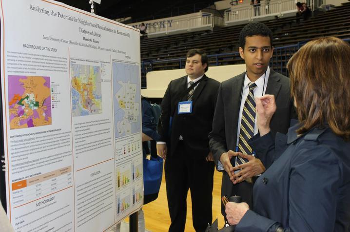 photo of male undergrad presenting research poster presentation to woman
