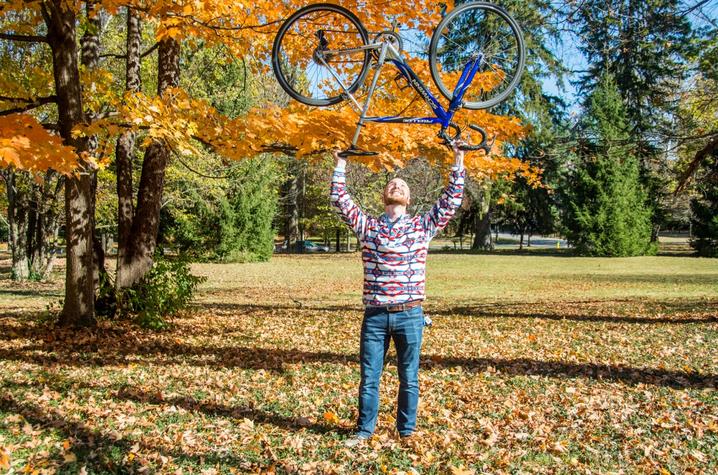 photo of Nate Williams holding bike over head with fall leaves - by Sally Horowitz Photography