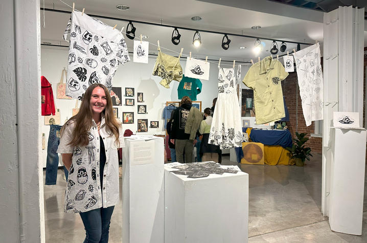 White woman in a white shirt and blue jeans standing next to artwork.