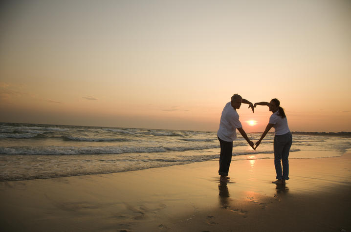 stock art photo of couple forming a heart with their arms on beach with sunset background