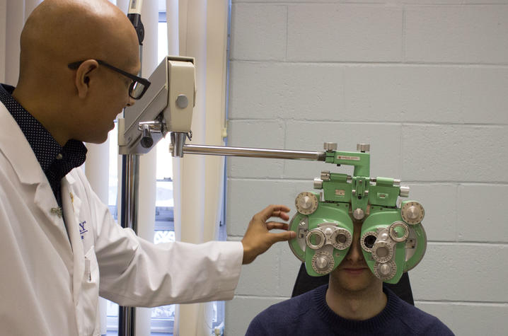 Paras Vora conducting an eye exam using a pale green phoropter