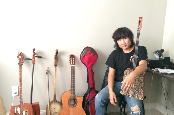 photo of Tamir Hargana seated by instruments and holding one