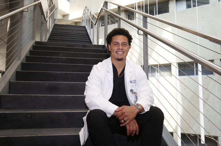 Dillon Powell in a white coat sitting on stairs