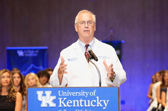 Older man standing at podium in white coat