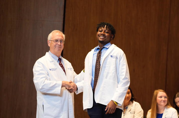 Photo of older man shaking hands with student in white coat