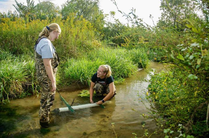 Two students in a creek conducting research 