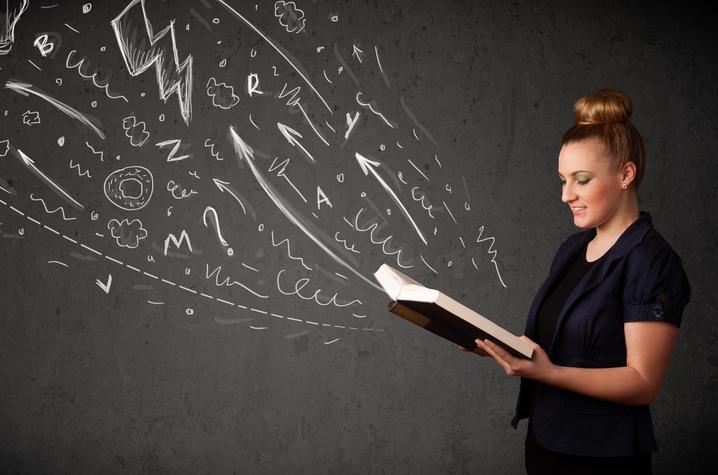 photo of woman with book open and drawings on chalkboard appearing to rise from it