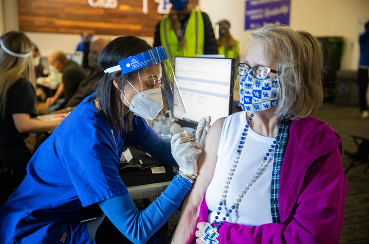 A lady wearing a UK mask and necklace receives a covid shot from a Health Sciences student