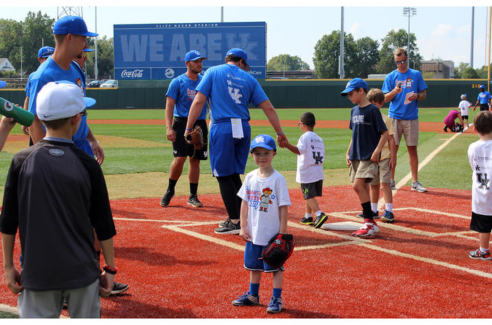 Jaxon Russell, wearing a white t-shirt and blue UK baseball hat, stands with his back facing the baseball field. 