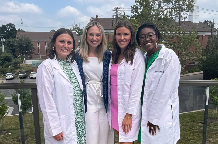 savannah jones standing and smiling in her white coat with some members of her PA cohort.
