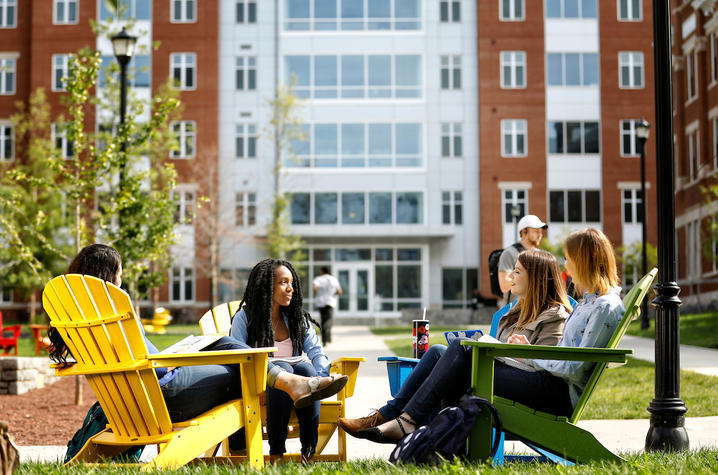 Three people sitting in chairs outside a residence hall.