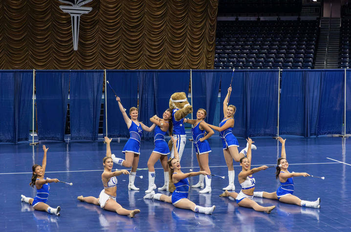 Team and mascot perform a choreographed routine with batons on a basketball court.
