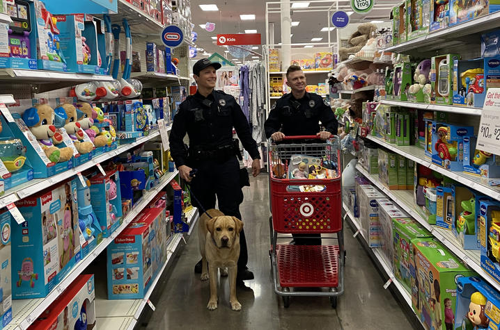 photo of two UK Police officers and the therapy dog in a toy aisle shopping for the Cram the Cruiser toy drive inn 2019