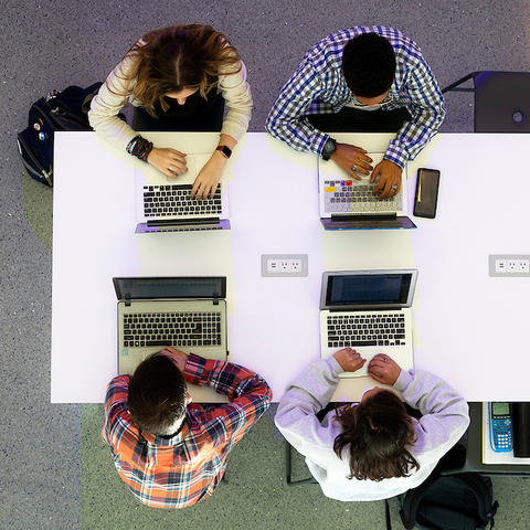 students on laptops sitting around a white table shot from above
