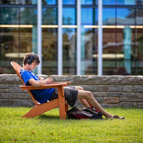 male student with headphones on sitting in an outdoor chair