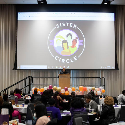 women speaking at podium at last year's Sister Circle Forum. 