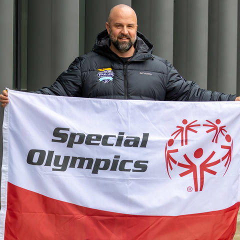 Capt. Adams standing, smiling, holding a Special Olympics flag in the student center