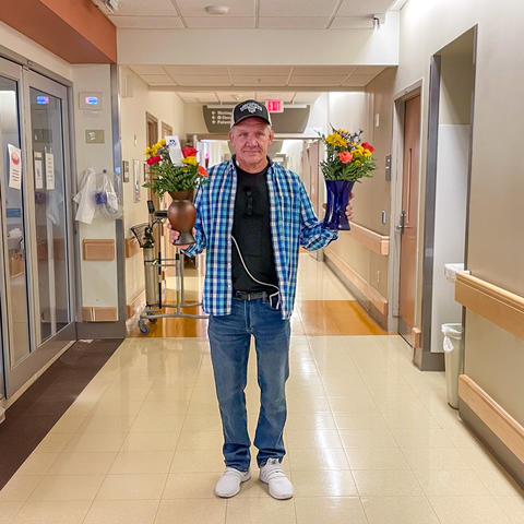 Image of Bobby Patton holding bouquets of flowers in a hospital corridor. 