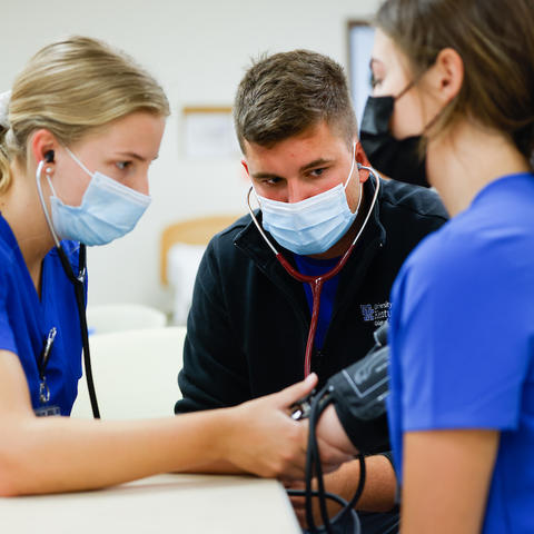 image of nursing student Colin Goodfellow watching other nursing students take blood pressure readings