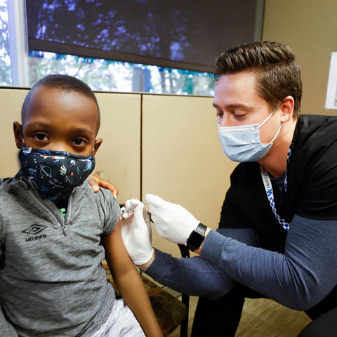 image of a pharmacist demonstrating the COVID-19 vaccine on a young boy.