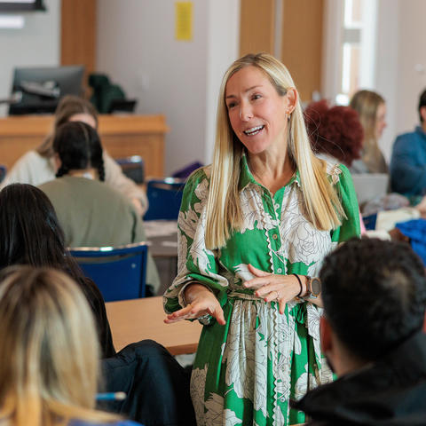 An instructor wearing a green dress talks to a group of students in a classroom.