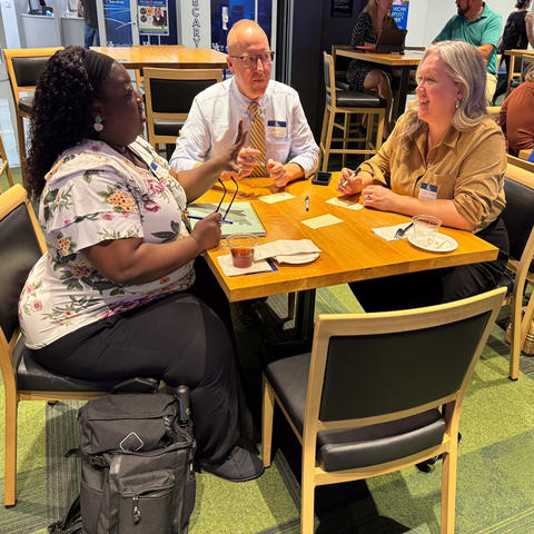 Three people — a Black woman, white man, and white woman, seated at a table. 