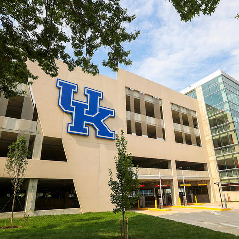 Exterior view of the University of Kentucky’s Sports Center Garage expansion, featuring a large blue UK logo on the parking structure beside a glass-enclosed stair tower.