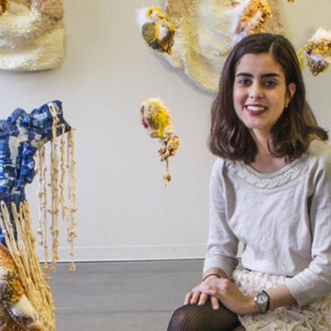photo of Amalia Galdona Broche seated in gallery with her art surrounding her