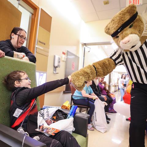 Child in hospital fist-bumping a person in a Wildcat mascot costume